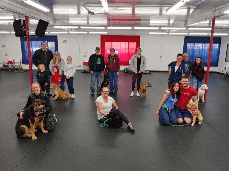 Families, including children, posing with their dogs on the training floor