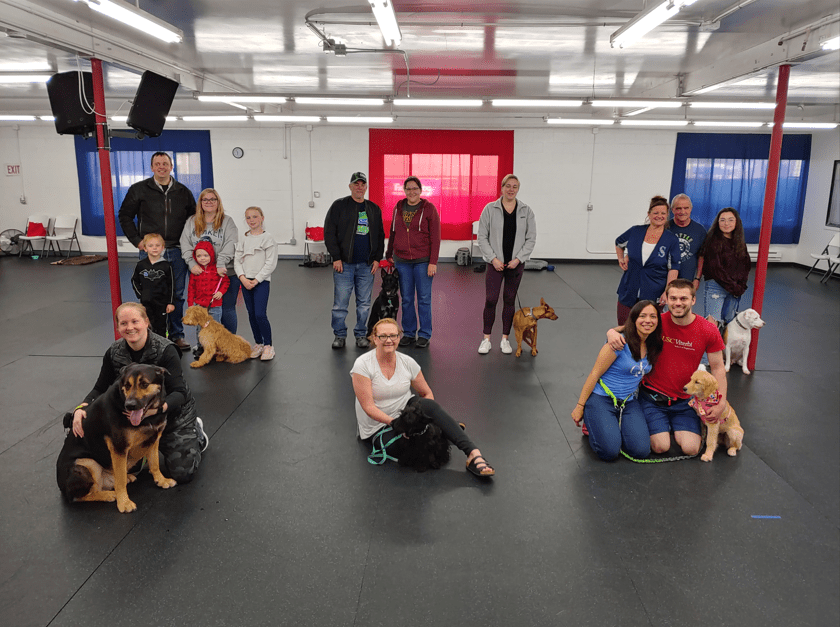 Families, including children, posing with their dogs on the training floor
